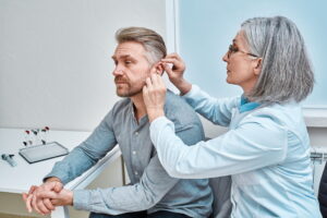 Experienced female doctor fitting Intra-The-Ear hearing aid into patient's ear while consultation in audiology clinic. ITE and ITC hearing aids Hearing Aid